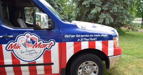 A red, white and blue ice cream truck is parked outside.