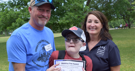 Dan, Danny and Deanna Rothbauer are smiling at the camera. Danny is holding a Shining Star certificate.