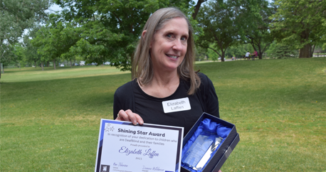 A white woman with light brown hair holds up a Shining Star certificate and glass award.A white woman with light brown hair holds up a Shining Star certificate and glass award.