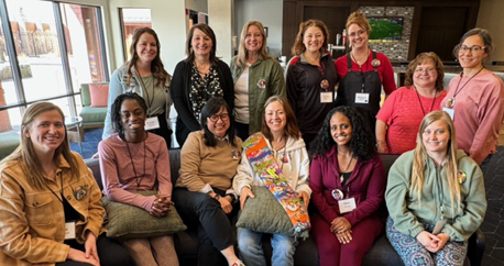 A group of 13 women are gathered together in a lobby smiling at the camera. These are moms who attended the MN DeafBlind Project Moms Retreat.