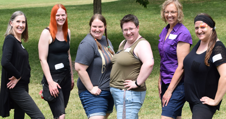 6 community interveners are standing with their hands on their hips and smiling at the camera at an outside park.